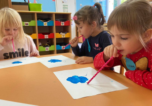 Zdjęcie przedstawia dzieci w trakcie rozdmuchiwania farby słomką